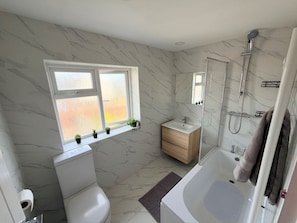 Un baño moderno con inodoro, lavamanos y ducha. Hay una ventana con plantas en el alféizar.