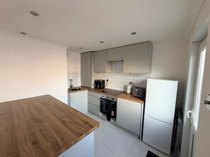 A modern kitchen with white cabinets, a wooden countertop, and stainless steel appliances. - House Sleeps 5 With Enclosed Garden (Corby)