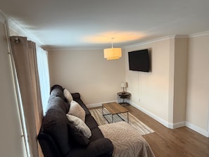 Una sala de estar con un sofá, una mesita, una lámpara y un televisor montado en la pared.