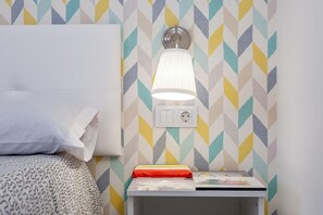 A neatly made bed with a pillow and a blanket, a bedside table with a lamp, a book, and a power outlet. - Apartment Near Las Cavellinas Beach (LA OLIVA FUERTEVENTURA)