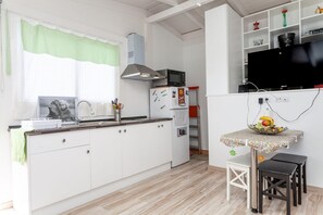 Una cocina compacta con armarios blancos, microondas y un pequeño comedor con mesa y taburetes.