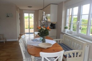 A dining area with a wooden table, white chairs, and a vase of flowers. - Holiday home with 1 bedroom (Wyk-Boldixum)