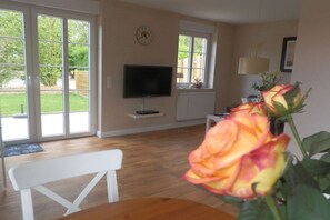 A room with a television, a bench, a table, a window with a view of greenery, and a clock on the wall. - Holiday home with 1 bedroom (Wyk-Boldixum)