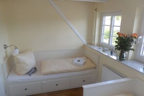 A room with a built-in bench with storage drawers, a window with a view of greenery, and a vase with flowers on the windowsill. - Holiday home with 1 bedroom (Wyk-Boldixum)
