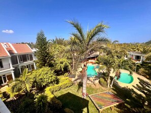 A residential area with a swimming pool, palm trees, and a multi-story building with a red-tiled roof. - Bazaar Square Lodges - Hibiscus (Garden) (Grand Baie)