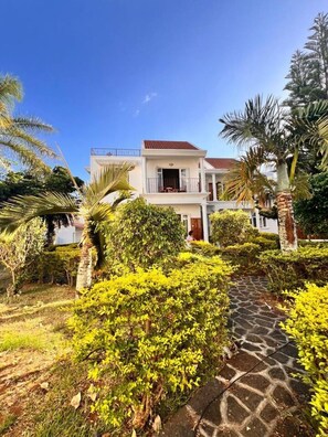 A two-story house with a balcony, surrounded by lush greenery and a stone pathway. - Bazaar Square Lodges - Hibiscus (Garden) (Grand Baie)