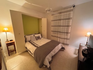 Une chambre à coucher avec un lit, des tables de chevet, un bureau et une fenêtre avec des rideaux.