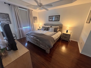 Une chambre à coucher avec un lit, des tables de chevet, un ventilateur de plafond et une fenêtre avec des rideaux.