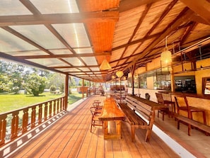 A covered outdoor seating area with wooden benches and tables, a bar counter, and a view of the outdoors. - Bazaar Square Lodges - Flamboyant (Upper Level) (Grand Baie)