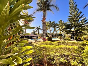 A tropical resort with palm trees, a swimming pool, and a building with a red roof. - Bazaar Square Lodges - Flamboyant (Upper Level) (Grand Baie)