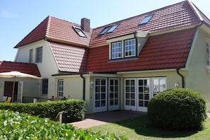 Ein zweistöckiges Haus mit rotem Ziegeldach, einer überdachten Veranda und einem gepflegten Rasen.