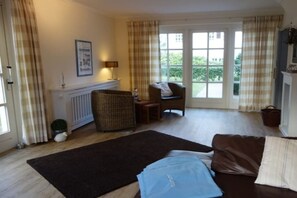 Een woonkamer met een bank, een stoel, een radiator, een raam en een deur.
