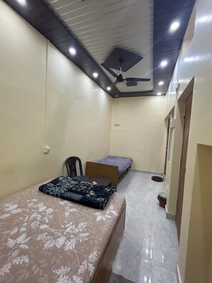 A small, compact room with a bed, a chair, and a desk. There is a ceiling fan and recessed lighting. - 5-bedroom bed & breakfast in brilliant Varanasi with AC (Varanasi)