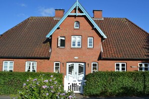 Ein rotes Backsteinhaus mit Satteldach, einer weißen Tür und einem kleinen Fenster.