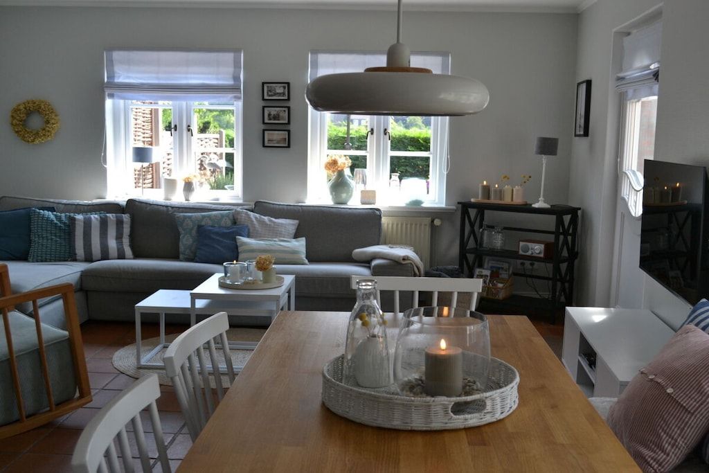 Un salon avec un canapé, une table à manger décorée d’une bougie et un luminaire suspendu.