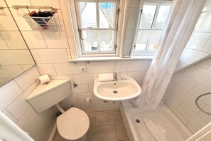 Un bagno compatto con WC, lavabo e vasca da bagno, una finestra con tende e un appendi asciugamani.