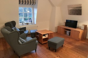 A living room with a sofa set, a television on a wooden stand, and a window with a view. - "Villa Friedericia" - Apt. 04 (Wyk auf Föhr)