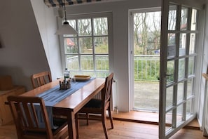 Ein Essbereich mit einem Holztisch, Stühlen und Blick durch eine Glastür auf eine Terrassenanlage.