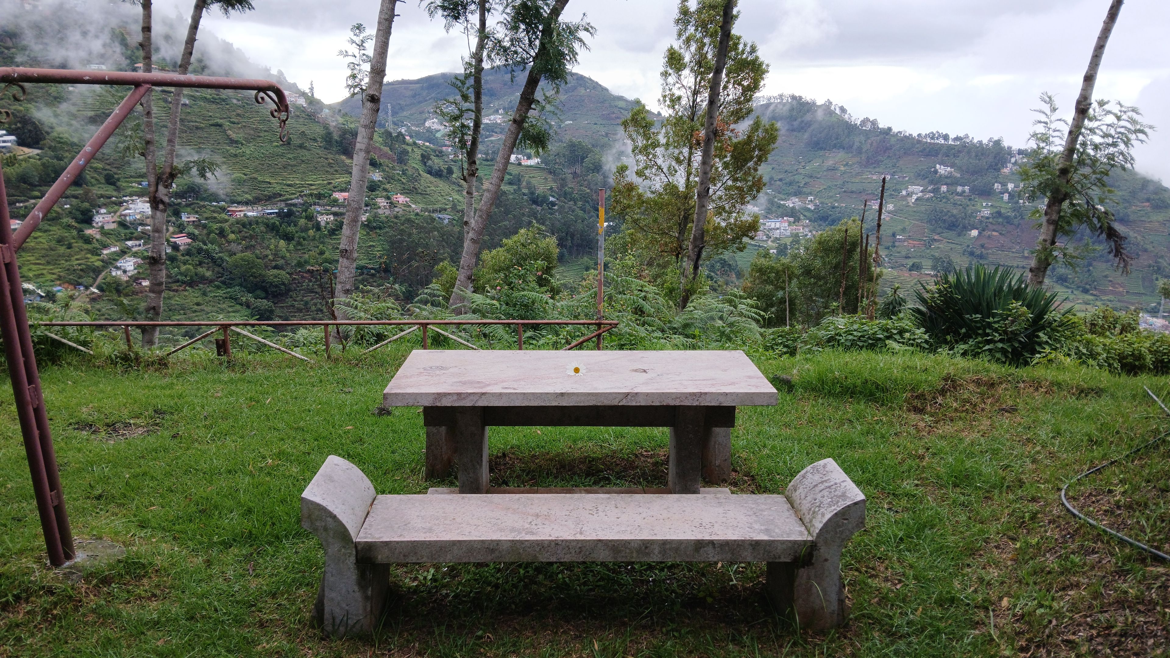 Mesa y banco de concreto en un área cubierta de césped, con montañas al fondo.