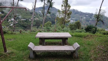 Mesa y banco de concreto en un área cubierta de césped, con montañas al fondo.