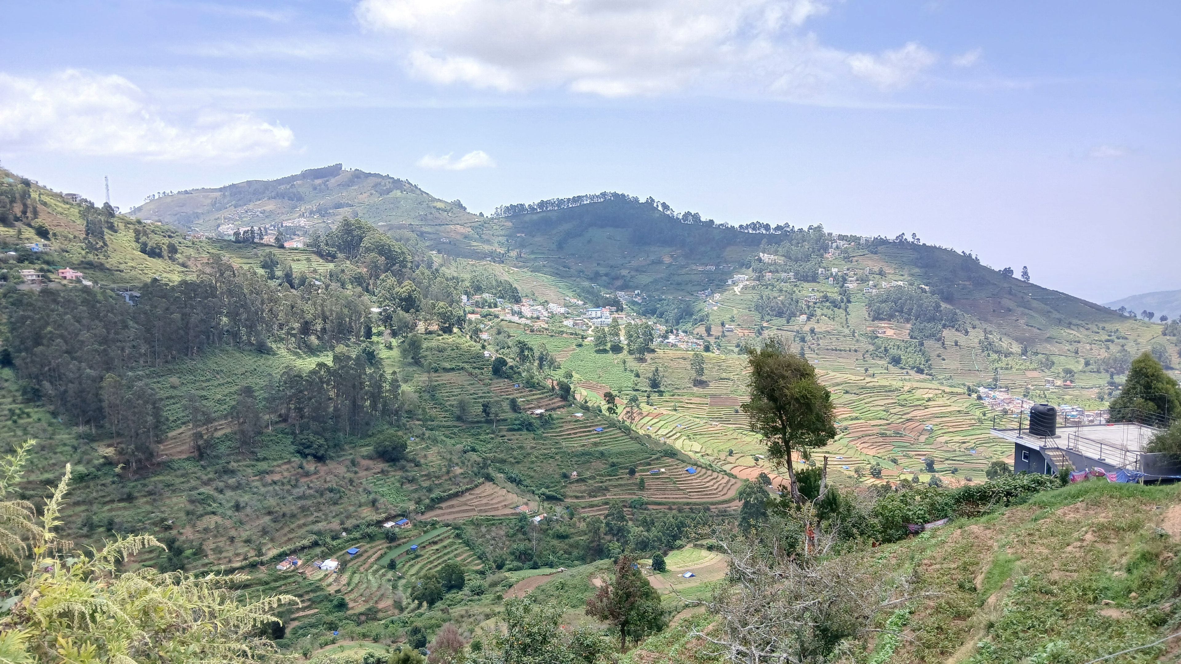Terraced agricultural fields, a few scattered buildings, and a prominent hill in the background.