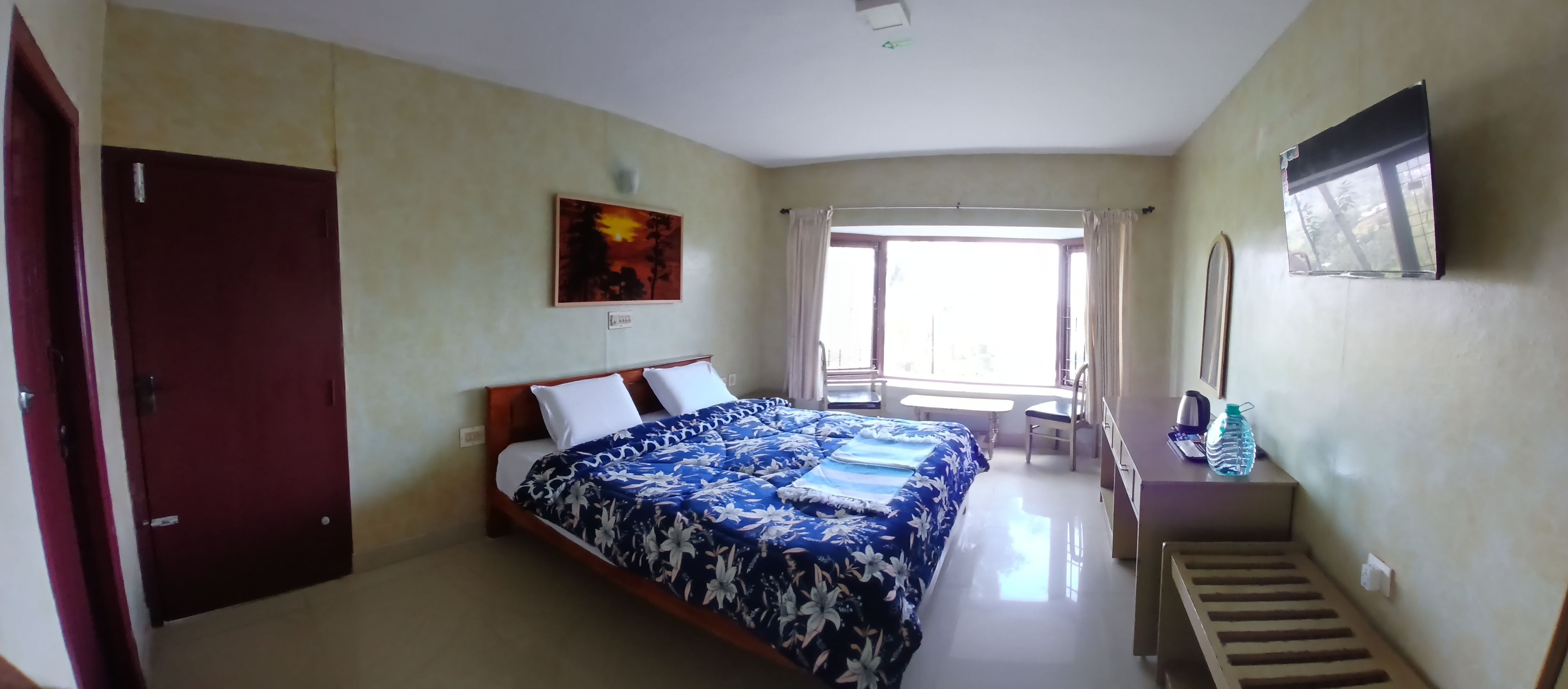 A bedroom with a bed, a desk, a chair, a water bottle, and a painting on the wall.