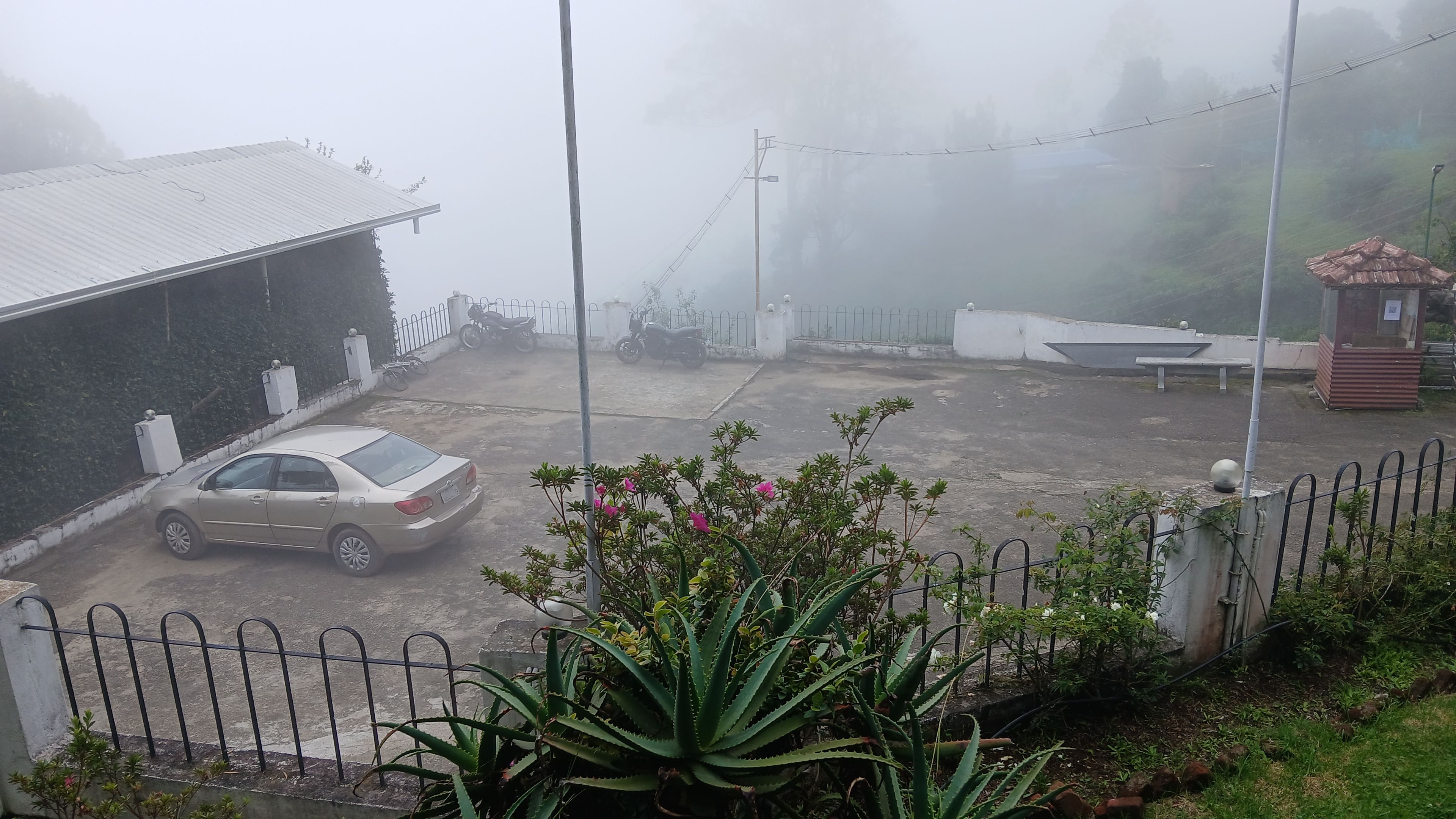 A foggy parking area with a car, a building, and a fence.