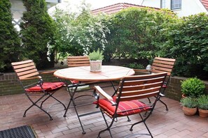 Une terrasse avec une table ronde et quatre chaises, entourée de plantes en pot et d’un mur en briques.