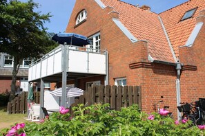 Ein Ziegelhaus mit einem Balkon, einem Holzzaun und rosa Blumen im Vordergrund.