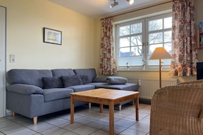 A living room with a grey sofa, a wooden coffee table, and a wicker chair. - "Haus Parkstrasse" - Apt. 01 (Wyk auf Föhr)