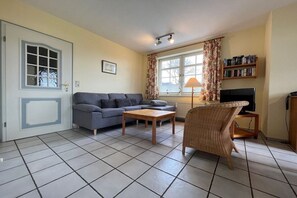 A living room with a sofa, a coffee table, a wicker chair, a television, and a bookshelf. - "Haus Parkstrasse" - Apt. 01 (Wyk auf Föhr)