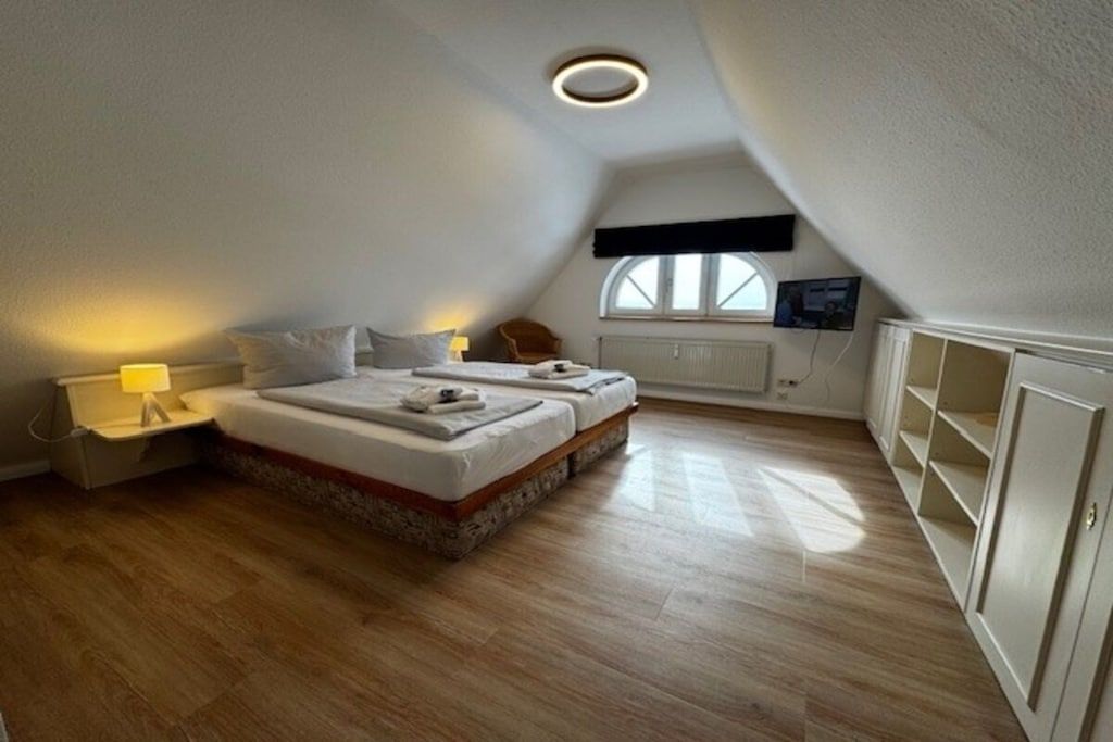 A bedroom with two beds, a window, a radiator, and a television.