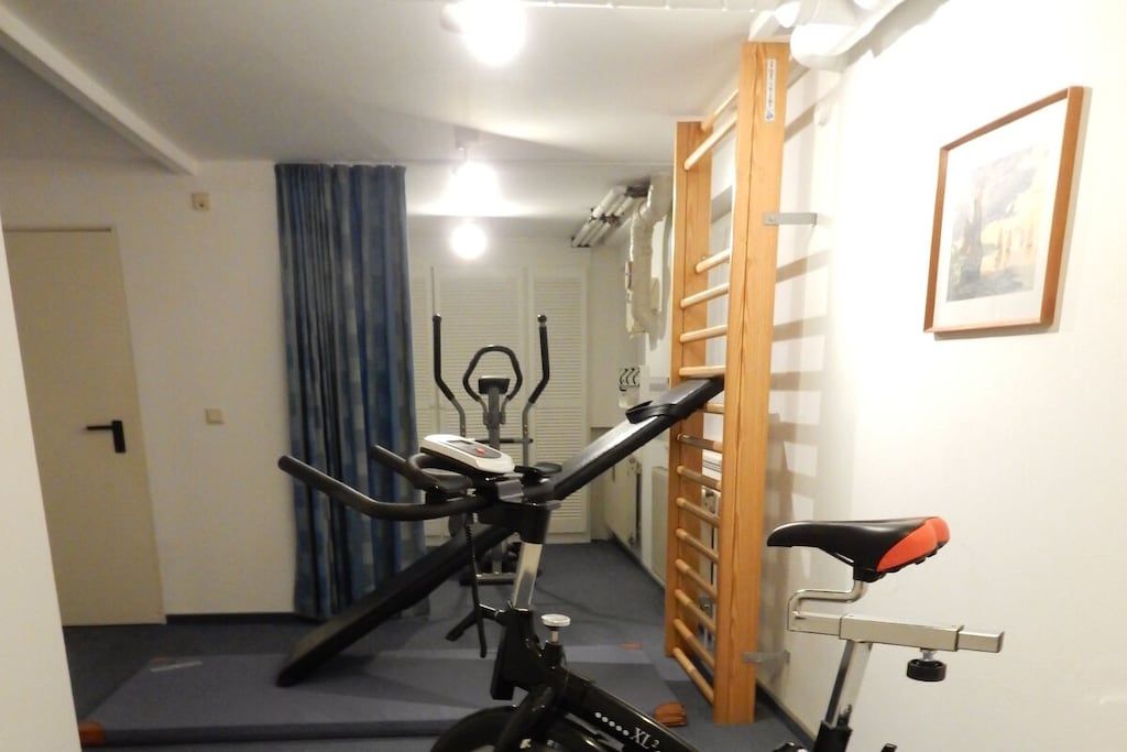 Ein Zimmer mit einem stationären Fahrrad, einer Tür, einem blauen Vorhang und einem gerahmten Bild an der Wand.