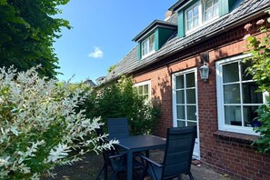 A brick house with a green roof, a window with a white frame, and a table with chairs in the foreground. - "Oldsum 2, House 94" (Oldsum)