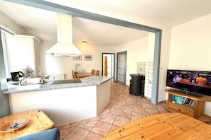 A compact kitchen with a central island, a dining area with a wooden table, and a television on a wooden stand. - "Oldsum 2, House 94" (Oldsum)