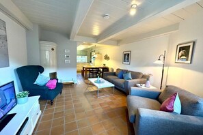 A living room with a sofa, armchair, coffee table, and a television on a stand. - Holiday apartment with 1 bedroom (Borgsum)