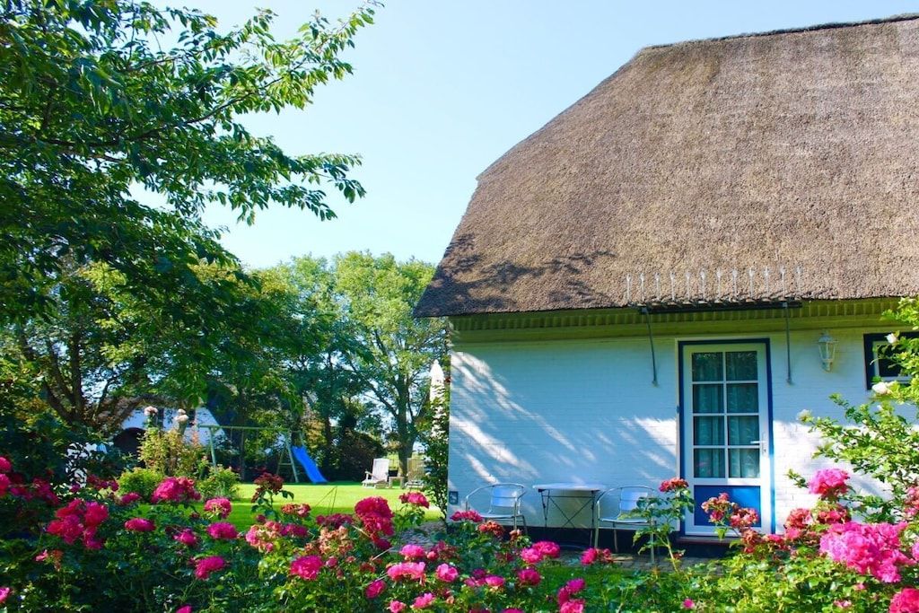 Ein Haus mit einem Strohdach, einer weißen Fassade und einem Garten mit rosa Blumen.