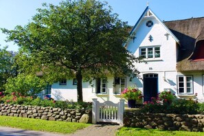 A traditional white building with a stone wall, a thatched roof, and a wooden gate. - Holiday apartment with 1 bedroom (Witsum)