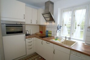 A kitchen with white cabinets, a stainless steel oven, a wooden countertop, a sink, and a window with curtains. - Holiday apartment with 1 bedroom (Witsum)