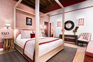 Un lit à baldaquin avec une couvre-lit rouge et blanche, une table de chevet en bois avec une lampe, un miroir rond et une chaise avec un coussin rouge.