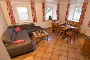 A cozy living room with a sofa, a dining table with chairs, and a window with curtains. - Holiday home with 2 bedrooms (Bischofsgrün)