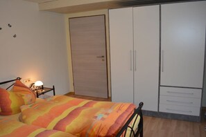 A bedroom with a bed, a nightstand with a lamp, a wardrobe with drawers, and a door. - Holiday apartment with 1 bedroom (Hopferau)
