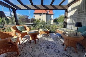 A balcony with wicker furniture, patterned floor tiles, and a view of a building with a red roof. - Alice's Holiday Apartment 2 (Arnstadt)