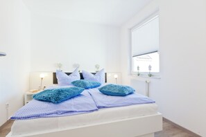 Ein Schlafzimmer mit einem Bett, Nachttischen, einem Fenster mit Jalousien und einer Heizung.