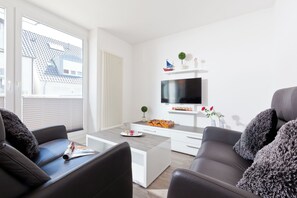 Ein modernes Wohnzimmer mit einer Couch, einem Couchtisch und einem an der Wand montierten Flachbildfernseher.