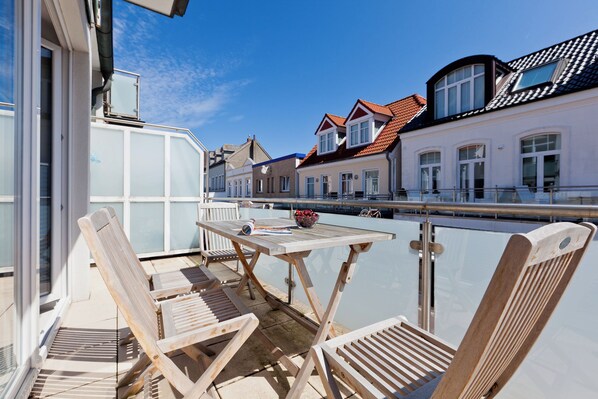 Eine Terrasse im Freien mit Holzmöbeln und einem Tisch, mit Blick auf einen Kanal und Gebäude im Hintergrund.
