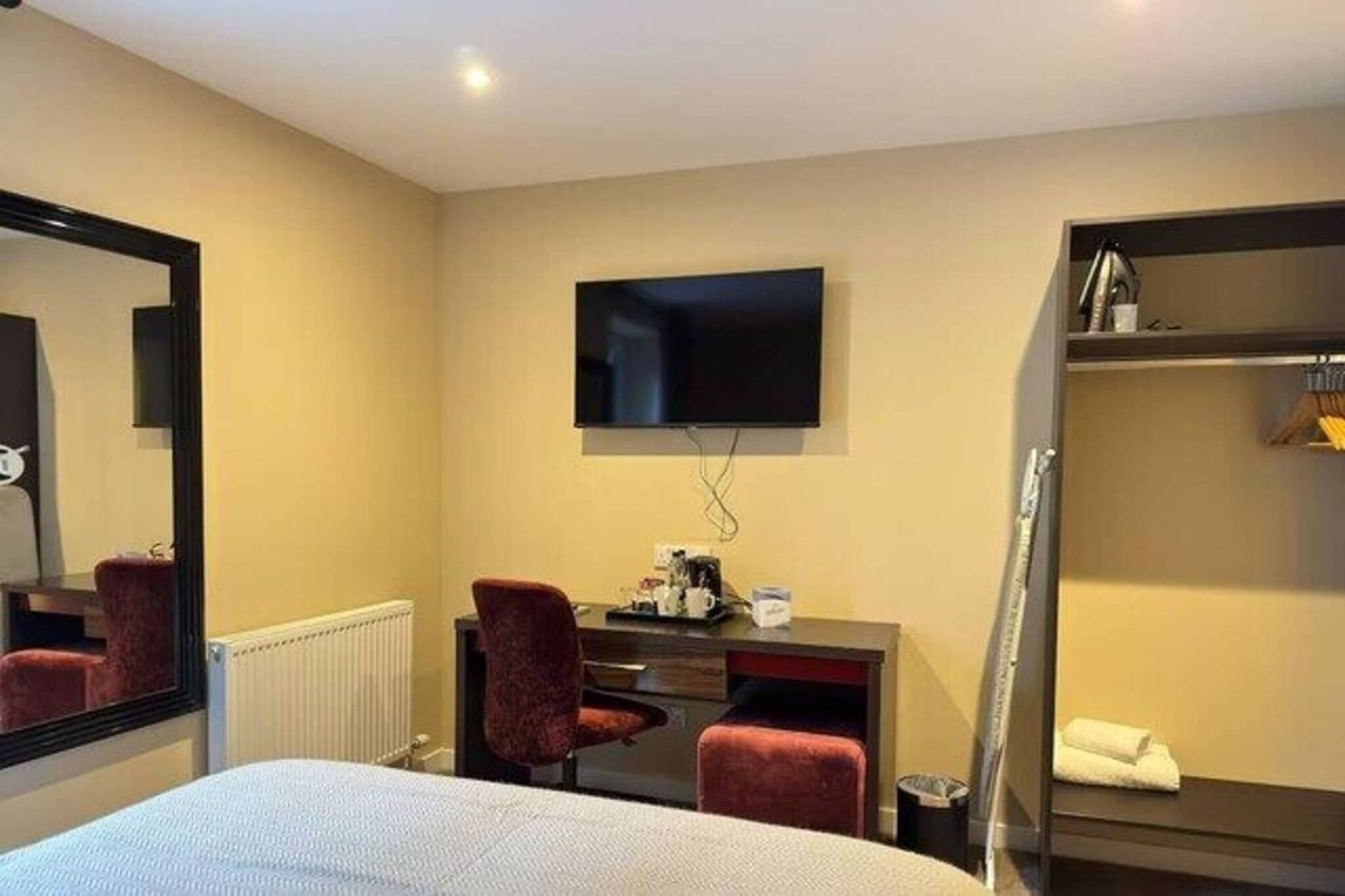 Een hotelkamer met een bed, een bureau met stoel, een aan de muur bevestigde televisie en een kledingkast.