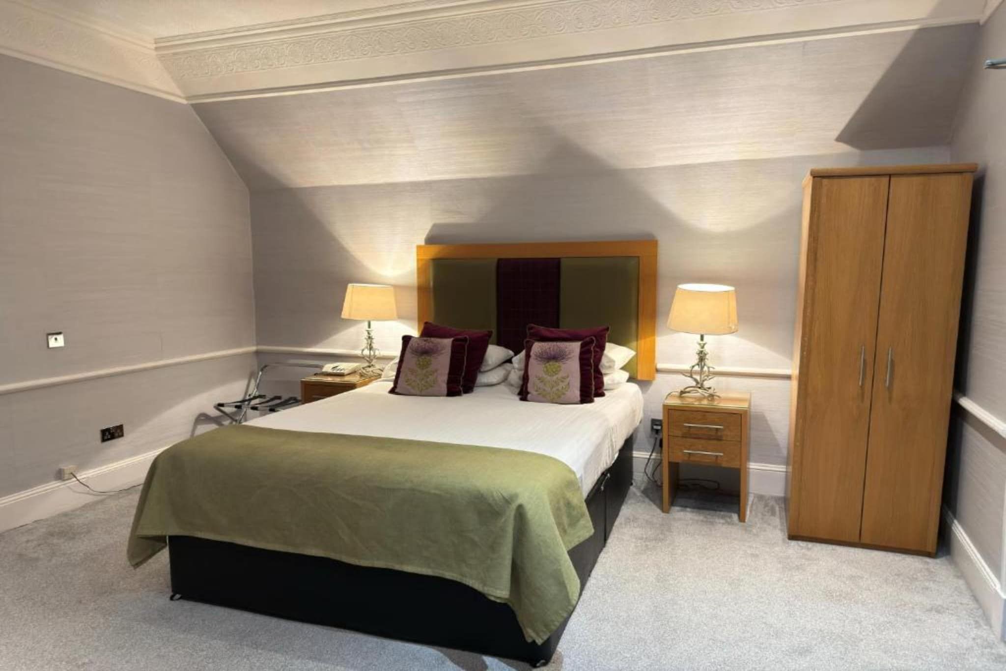 A bedroom with a bed, two bedside tables, a wardrobe, and a ceiling with a sloped design.