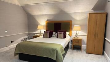 A bedroom with a bed, two bedside tables, a wardrobe, and a ceiling with a sloped design.
