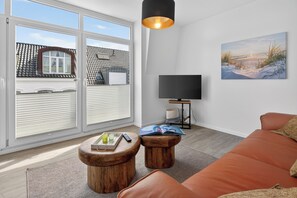 Ein modernes Wohnzimmer mit einer Couch, Holztischen, einem Flachbildfernseher und einem Bild an der Wand.